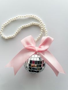 a disco ball ornament with a pink bow and pearls on a white background