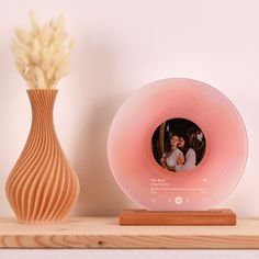 a wooden vase with a white flower next to a pink photo frame on a shelf