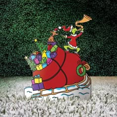 a christmas sleigh with presents on it in front of a green wall and bushes