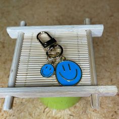 a blue smiley face keychain sitting on top of a wooden shelf next to a green vase