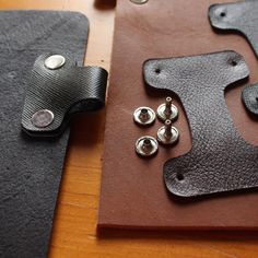 two pieces of leather with metal buttons on them sitting on top of a wooden table