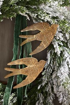 two gold fish ornaments hanging from a green christmas tree with snow on the ground and evergreen branches