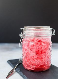 a glass jar filled with red liquid sitting on top of a black slate board next to a knife