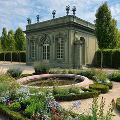 a green building surrounded by lots of flowers and greenery in the middle of a garden