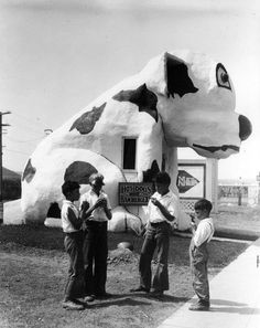 black and white photograph of three boys standing in front of a cow shaped building that looks like a house