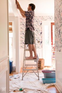 a man standing on a ladder painting the walls in a room with floral wallpaper