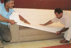 two men unpacking a couch in a living room with red carpet and white walls