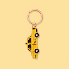 A gold keychain that looks like a New York taxi hangs from a brass ring.  The taxi is yellow with black wheels and windows. The tires have a white circle in the middle.  The background is a soft yellow color. Nyc Keychain, Keychain Souvenir, Yellow Taxi, Lets Roll, Key Organizer, The Big Apple, Keychain Bag, City That Never Sleeps, Big Apple