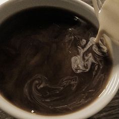 a white bowl filled with brown liquid next to a cup of coffee on top of a wooden table