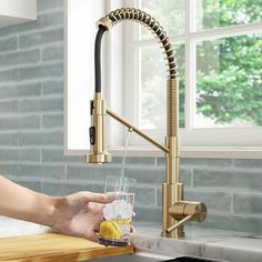 a person holding a glass in front of a kitchen faucet with water running from it