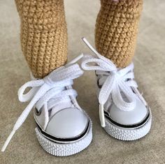 the legs and feet of a crocheted doll wearing white shoes with laces