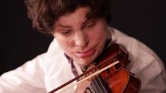 a young man is playing the violin in front of his face and looking down at it