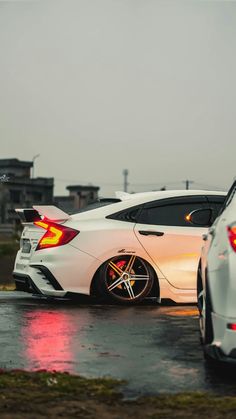 two white cars parked next to each other on a wet parking lot