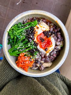 a person holding a bowl of food with broccoli and other foods in it