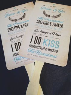 two fan shaped wedding programs on top of a wooden paddle with blue ink and white lettering