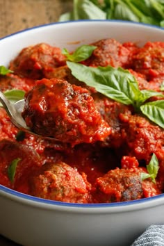 a bowl filled with meatballs covered in marinara sauce and garnished with basil