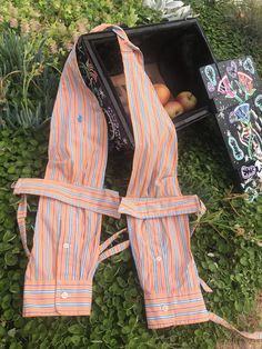 an orange and blue striped apron sitting on the ground next to a box with fruit in it