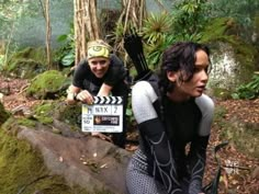 two men in wetsuits crouching next to each other near rocks and trees