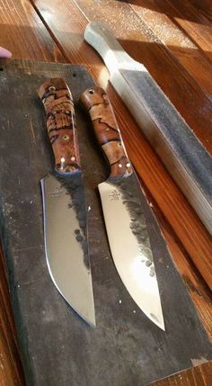 two knives on a cutting board next to a knife sharpener and an open knife blade