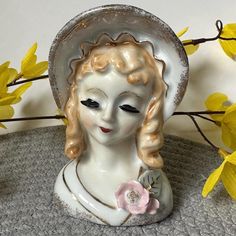 a white ceramic figurine with a hat on it's head and flowers in the background