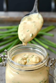 a spoon full of mayonnaise on top of a jar with asparagus in the background