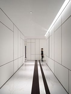 a person walking down a long hallway with white walls and black stripes on the floor