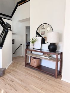 an entryway with a wooden table and black vase on it, next to a staircase