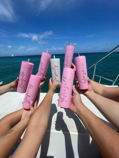 four people holding cups with writing on them while sitting on a boat in the ocean