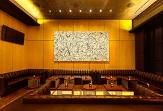 a large painting hangs on the wall in a restaurant with leather booths and wooden tables