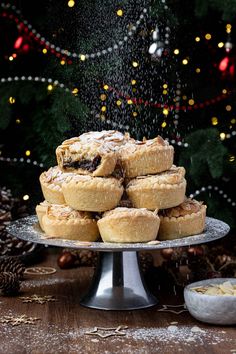 a pile of pies sitting on top of a cake plate next to a christmas tree