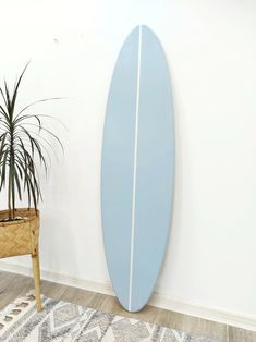 a blue surfboard leaning up against a white wall next to a potted plant