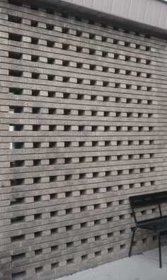 a bench sitting in front of a brick wall with holes on it's side