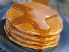 a stack of pancakes on a plate with syrup drizzled over them and two glasses of orange juice in the background