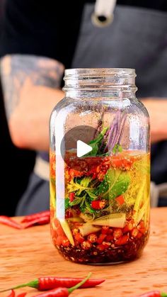 a glass jar filled with food sitting on top of a wooden table next to red peppers