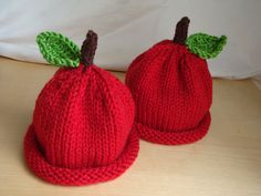 two knitted red apples sitting on top of a wooden table next to each other