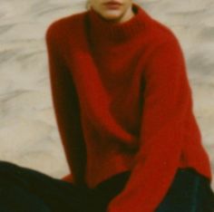 a woman sitting on the ground wearing a red sweater