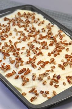 a pan filled with white frosting and pecans sprinkled on top of it