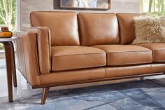 a tan leather couch with pillows on it in a living room area next to a table