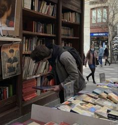 a man is looking at books in a book store on the sidewalk with people walking by