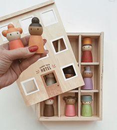 a hand holding a wooden dollhouse with several small dolls in it's box