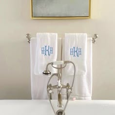 two white towels are hanging on the wall above a bathtub in front of a painting