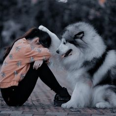 a woman kneeling down next to a dog with its head on her hand and it's mouth open