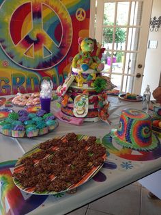 a table topped with cakes and cupcakes covered in frosting next to a peace sign