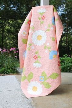 a pink and green flowered quilt hanging on the side of a wooden pole in front of some trees