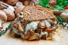 a grilled cheese and mushroom sandwich on a wooden cutting board with mushrooms in the background