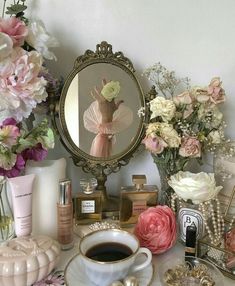 a cup of coffee sitting on top of a table next to a mirror and flowers