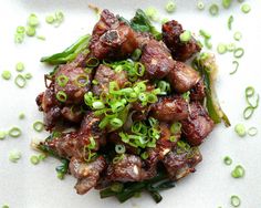 a white plate topped with meat and veggies on top of green onions next to broccoli