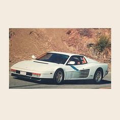 a white sports car driving down the road in front of a mountain side area with no one around it