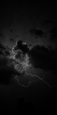 a black and white photo of lightning in the night sky with dark clouds behind it