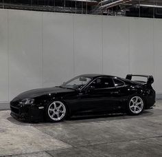 a black sports car parked in front of a white wall with chrome rims on it